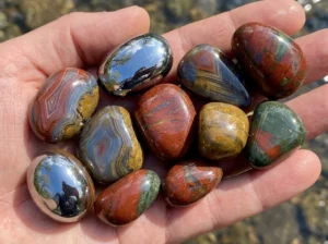 Close-up of highly polished Agate and Jasper stones held in a hand, showing the high-gloss shine achieved by tumbling rocks of identical Mohs hardness.
