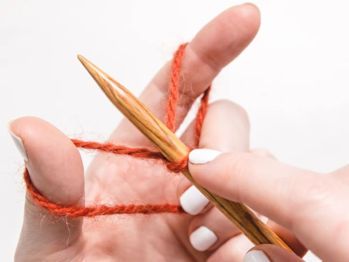 Hands holding yarn in the slingshot position for a long-tail cast-on.