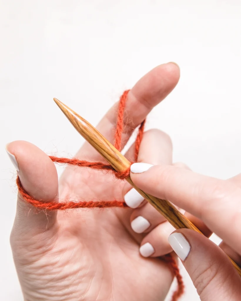 Hands holding yarn in the slingshot position for a long-tail cast-on.