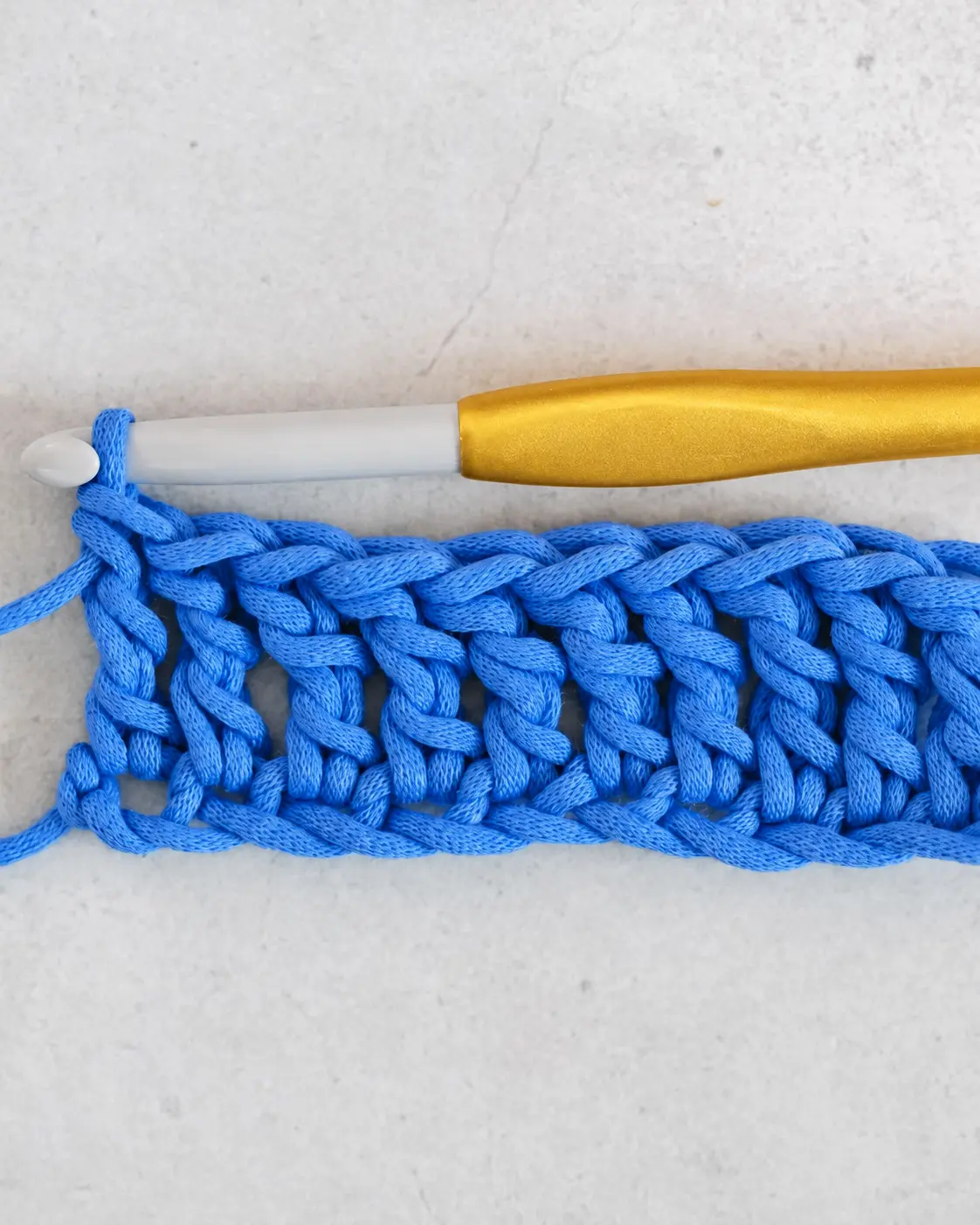 First row of sage treble crochet with a marker at each edge and a rose-gold hook in the live loop.