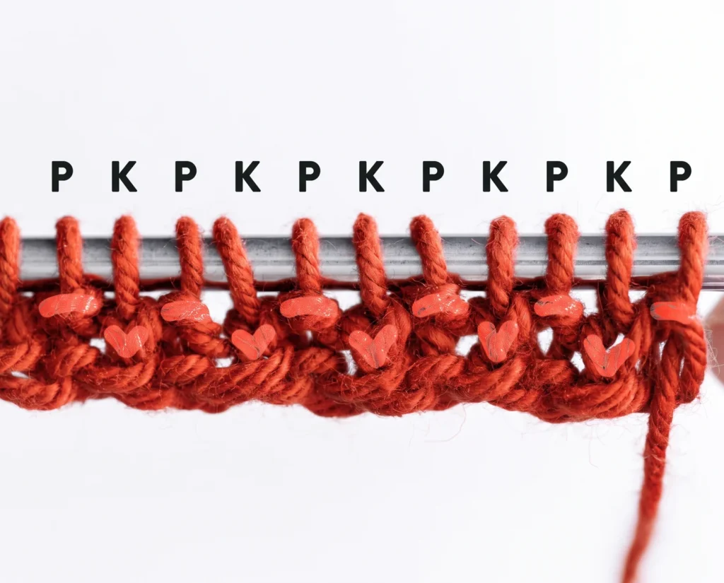 Close-up of rust-orange stitches on a needle marked P and K above alternating purl and knit stitches